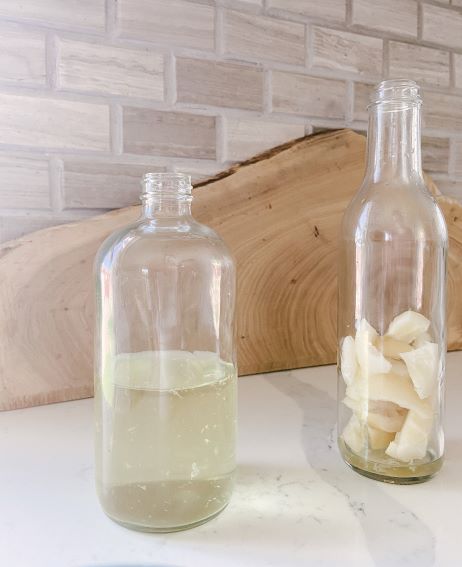 clear glass spray bottle half filled with lemon vinegar and emply glass bottle filled with lemon peels