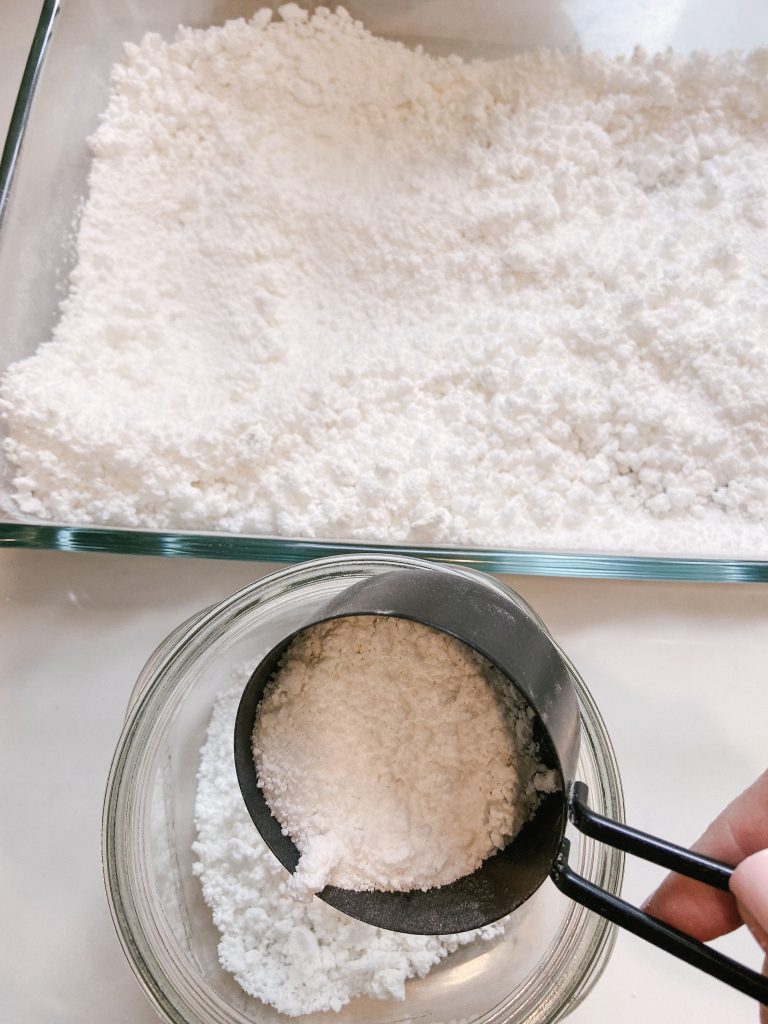 scooping out finished homemade dishwasher powder from glass pan into glass jar