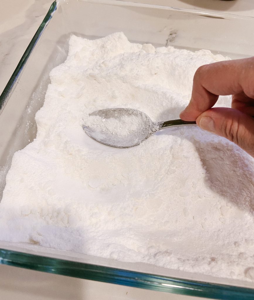 mixing dishwasher detergent powder in glass pan with a stainless steel spoon