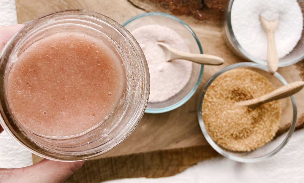 pink himalayan body scrub in glass jar with pink salt, raw sugar and coconut sugar in bowls